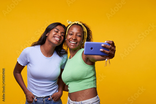 Photographie Portrait of cool cheerful girl having video call with lover holding smart phone in hand shooting selfie on front camera isolated on yellow background enjoying happy moment