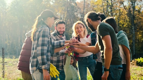 Caucasian team of males and females, volunteers with child putting hand on hand in circle and making gesture of cooperation and coworking. Successful work together concept. Eco activists. Outdoors.