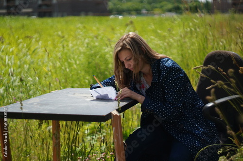 A young woman is working outdoors. She is working with a paper and pen, without laptop. She is happy and relaxed and smiling.