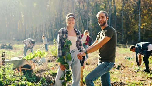 Obraz na plátně Portrait of young Caucasian happy couple of eco activists smiling to camera in park on sunny day and planing seedling of tree on field in forest or park
