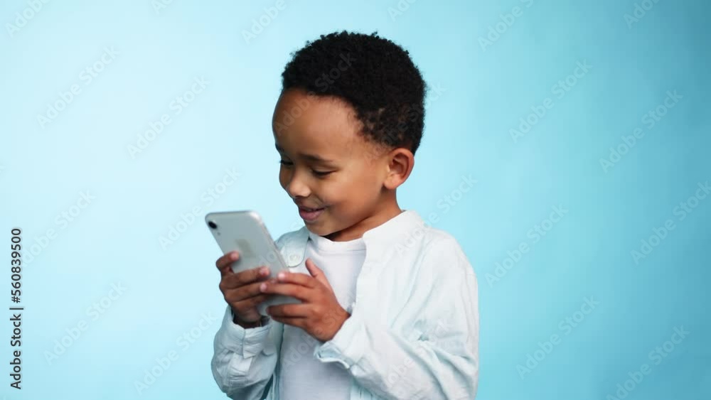 Adorable cute african american little boy child kid hold smartphone scrolling social media use educational children app application or play game on isolated blue background Adorable cute african american little boy child kid hold smartphone scrolling social media use educational children app application or play game on isolated blue background