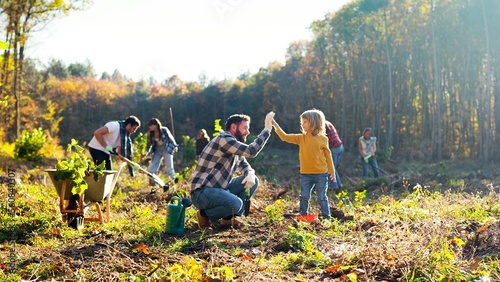 Little Caucasian cute boy helping her father to plant tree in forest or garden on sunny fall day. Outdoors. Man with small daughter planting seedling in wood or park. Environment activism.