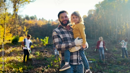 Portrait shot of happy caucasian handsome father holding small cute pretty daughter on hands and smiling cheerfully to camera in garden. Outdoor. Dad with child, eco activists.