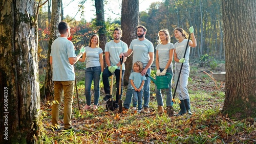 фотографія Man curator of eco activists standing with document or plan in hands and giving orders to people for planting trees in garden or forest