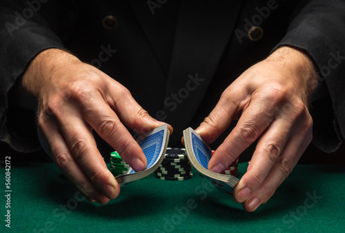 Professional dealer or croupier shuffles playing cards in a club at a green table with playing chips. The concept of a successful poker game in a casino