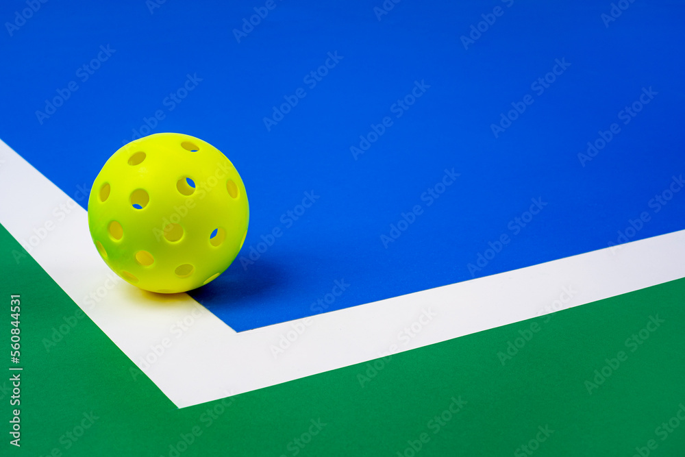 Indoor Pickleball on the court line. Yellow Pickleball with Blue