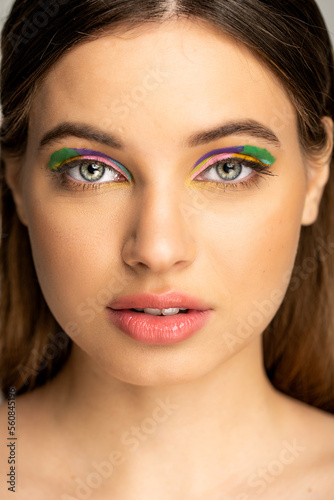 Teenage girl with colorful makeup looking at camera isolated on grey.