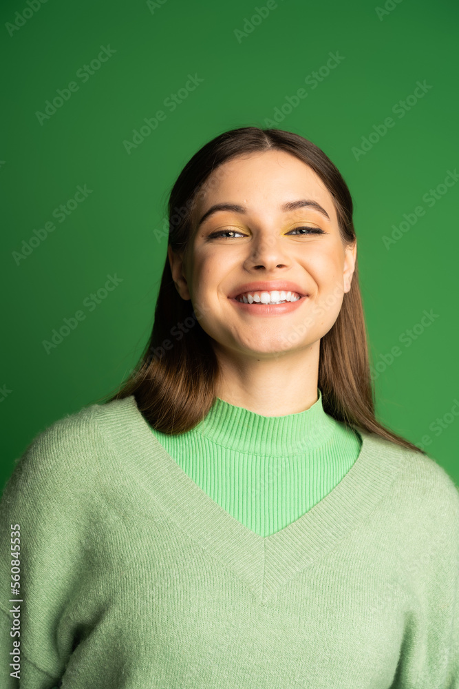 Fototapeta premium Portrait of happy teen girl in jumper smiling at camera isolated on green.