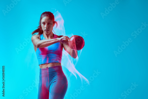 A female bodybuilder lifting kettlebell in studio. Long exposure movement capture.