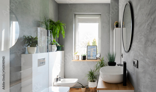 Modern interior of bathroom with stylish design. Ceramic washbasin and round mirror on the grey wall. Simple style and scandinavian decor in bathroom.