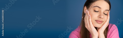 Pretty teenage girl touching face isolated on blue, banner.