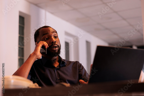 Financial analyst discussing company report with colleague on smartphone, african american man answering teamlead mobile call. Corporate worker having telephone conversation in coworking space photo