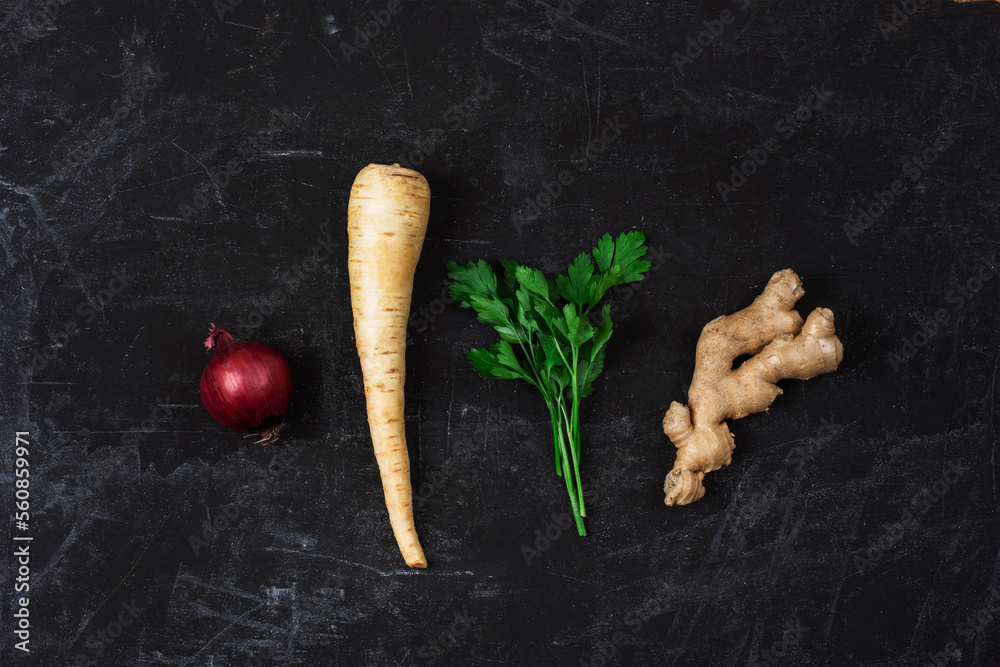 Red onion, parsnip root, ginger and parsley on black textured background. Minimal composition. Top view, flat lay