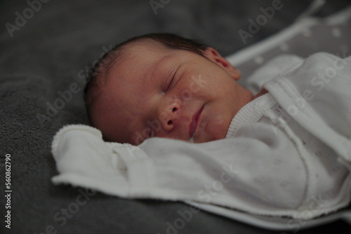 Newborn baby smiles during his sleep. The baby boy has just eaten and has some milk on his mouth. He is dressed in white clothes. High quality photo