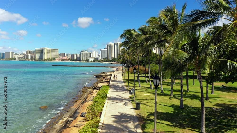 Lockdown Shot Of People Walking On Promenade By Blue Sea Against Building During Sunny Day - Oahu, Hawaii Lockdown Shot Of People Walking On Promenade By Blue Sea Against Building During Sunny Day - Oahu, Hawaii