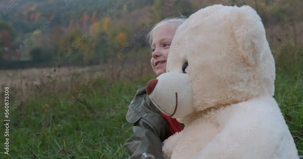 Portrait of little fair-haired girl hugging large teddy bear. Blonde child plays soft toy in nature in autumn Portrait of little fair-haired girl hugging large teddy bear. Blonde child plays soft toy in nature in autumn