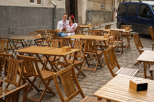 a young couple in Ukrainian national clothes  an embroidered woman sitting at a wooden table on the street  a terrace in a cafe