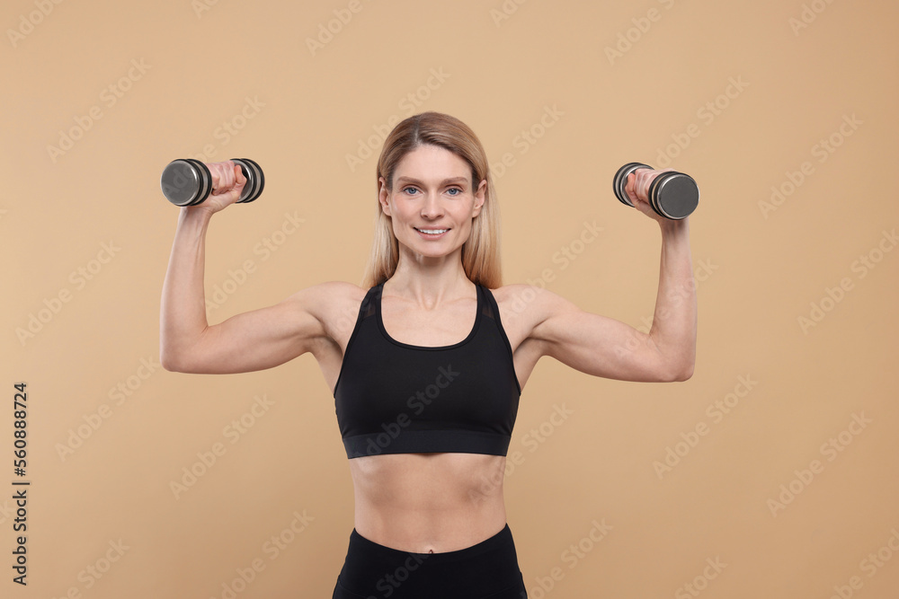 Portrait of athletic woman exercising with dumbbells on beige background Portrait of athletic woman exercising with dumbbells on beige background