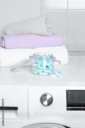 Jar with water softener tablets near stacked towels on washing machine photo