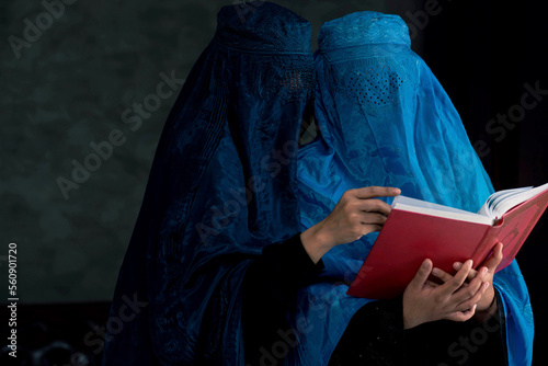 Two Afghan Muslim women with burka traditional costume, reading holy Quran against the dark background photo