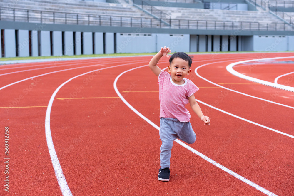 A boy in a sportswear and sneakers runs on the running track at the stadium outdoors.