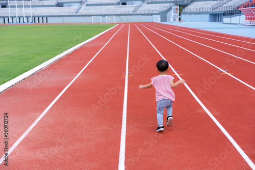 A boy in a sportswear and sneakers runs on the running track at the stadium outdoors.