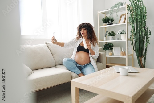 A pregnant woman blogger advertises a cream for pregnant women from stretch marks on the body during pregnancy filming herself on the phone while sitting on the couch at home freelancer