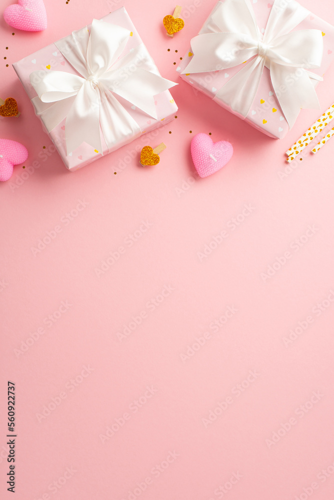 Valentine's Day concept. Top view vertical photo of present boxes with ribbon bows decorative clips heart shaped candles straws and golden sequins on isolated pastel pink background with empty space