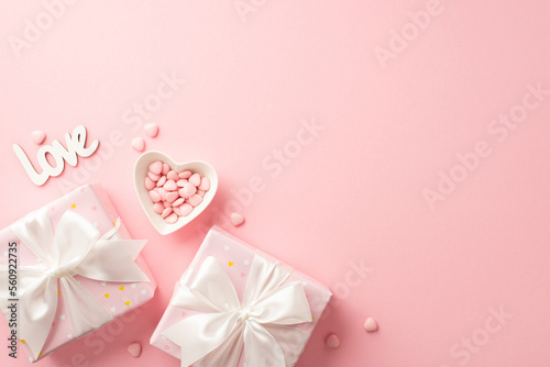 Valentine's Day concept. Top view photo of present boxes with white ribbon bows heart shaped saucer with sprinkles and inscription love on isolated pastel pink background with copyspace © ActionGP