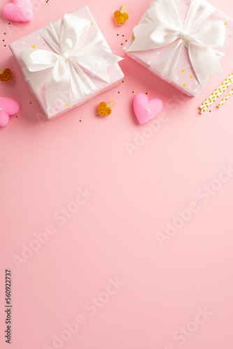 Valentine's Day concept. Top view vertical photo of present boxes with ribbon bows decorative clips heart shaped candles straws and golden sequins on isolated pastel pink background with empty space © ActionGP