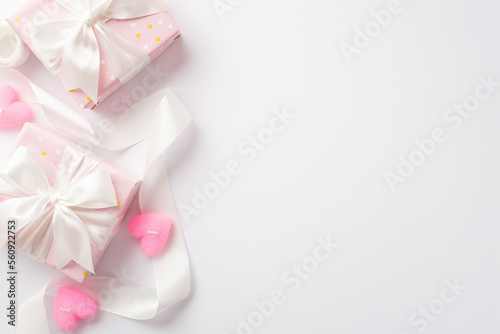 Valentine's Day concept. Top view photo of pastel pink gift boxes curly silk ribbon and heart shaped candles on isolated white background with copyspace
