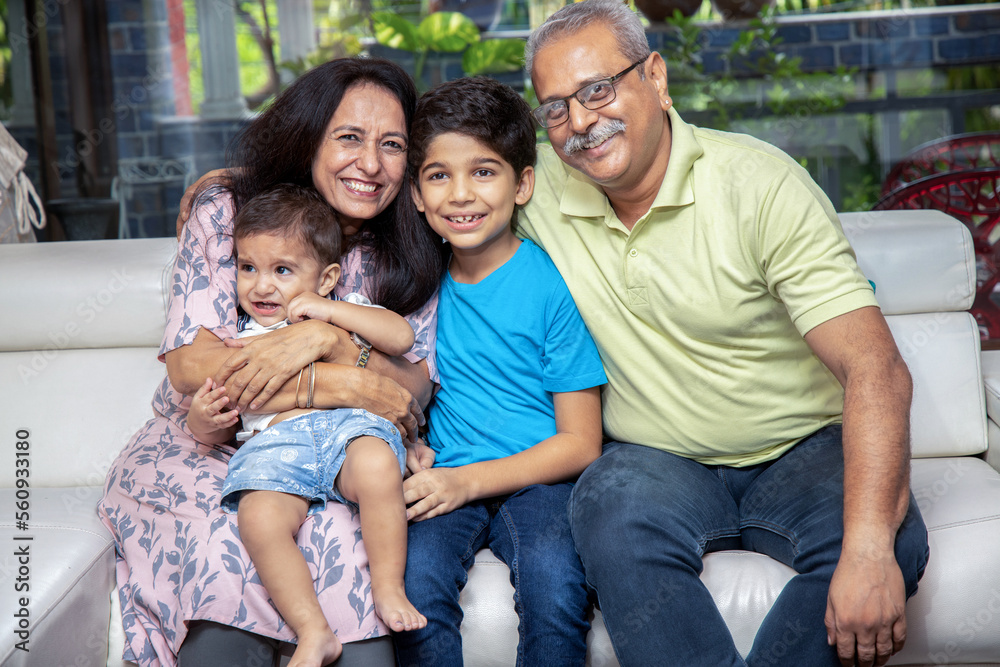 Portrait of Happy indian grand parents sitting with their grand children at home. Asian senior and young couple with kids looking at camera.