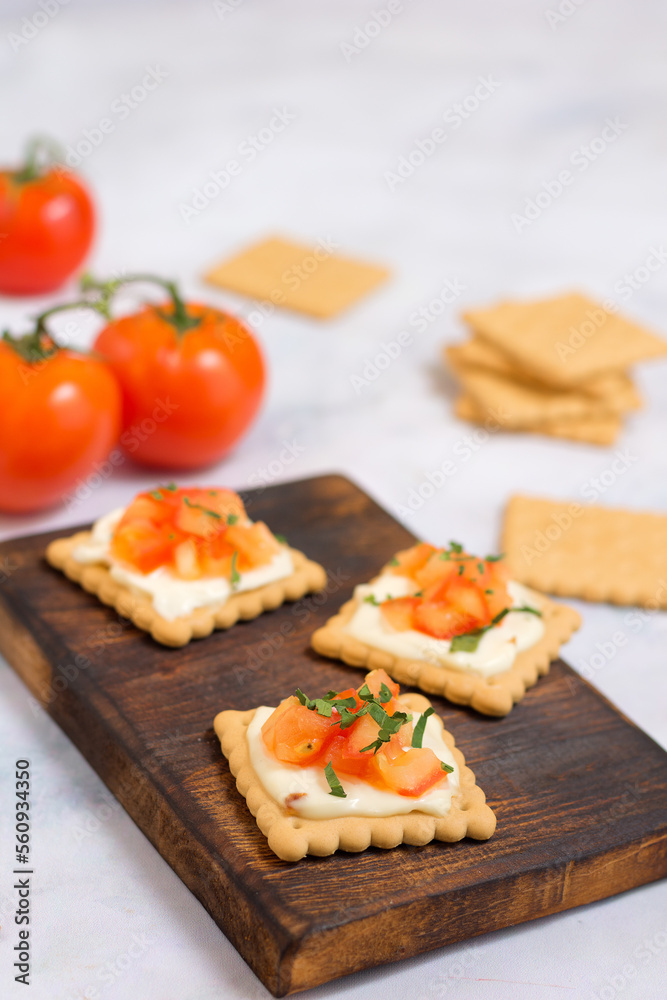 Quick cooked appetizer of cream cheese on a cracker with tomato and herbs on a wooden dark board and a light background Quick cooked appetizer of cream cheese on a cracker with tomato and herbs on a wooden dark board and a light background