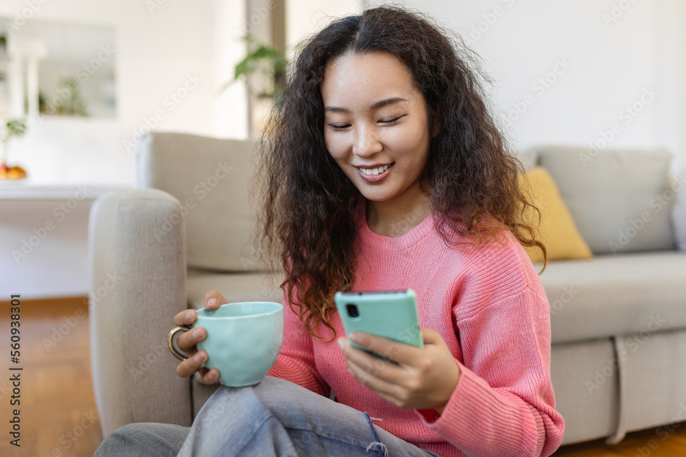 Attractive smiling Asian woman using smart phone while sitting on the sofa at home. Communication and video call concept. Attractive smiling Asian woman using smart phone while sitting on the sofa at home. Communication and video call concept.