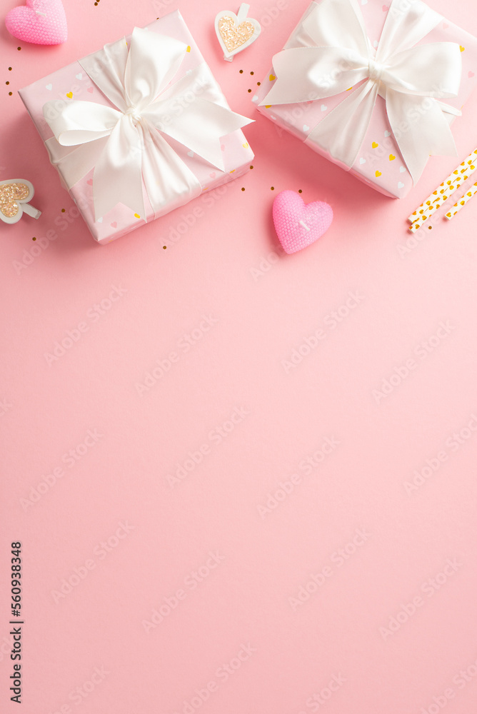 St Valentine's Day concept. Top view vertical photo of gift boxes with ribbon bows decorative clips heart shaped candles straws and golden sequins on isolated light pink background with empty space