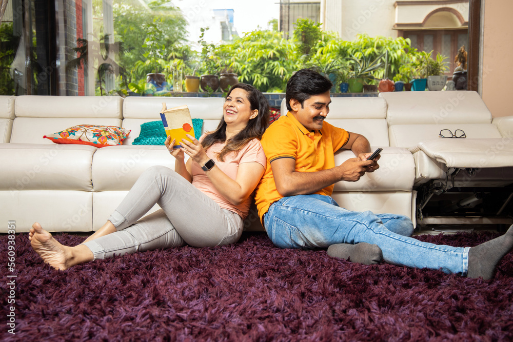 Portrait of happy young indian couple sitting on floor book and using smart phone at home reading Asian husband and wife spend time with each other, Full length shot. Portrait of happy young indian couple sitting on floor book and using smart phone at home reading Asian husband and wife spend time with each other, Full length shot.