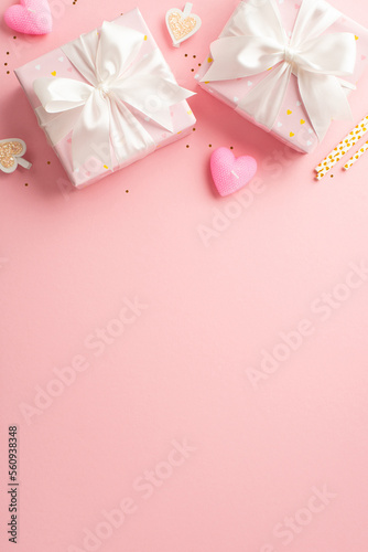 St Valentine's Day concept. Top view vertical photo of gift boxes with ribbon bows decorative clips heart shaped candles straws and golden sequins on isolated light pink background with empty space © ActionGP
