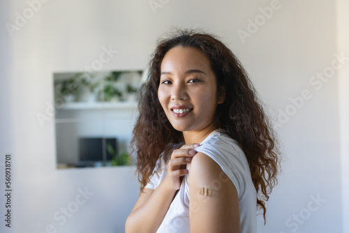 Woman pointing at her arm with a bandage after receiving the covid-19 vaccine. Asian woman showing her shoulder after getting coronavirus vaccine