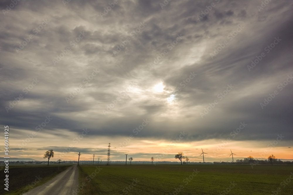 gray clouds on the sky with sun in a flat landscape with windmills