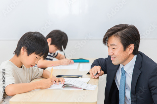 小学生に授業で勉強を教える笑顔の塾講師・先生（夏期講習・日本人男性） 