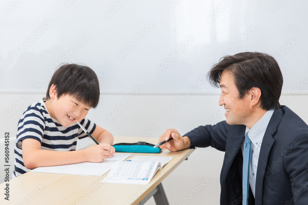 小学生に授業で勉強・漢字を教える笑顔の個別指導の塾講師・先生（日本人男性）
