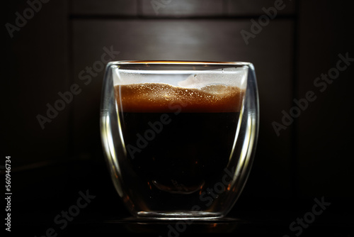 Foam layer of an espresso coffee in a double-walled glass cup against dark background. Coffee industry concept close up photo.