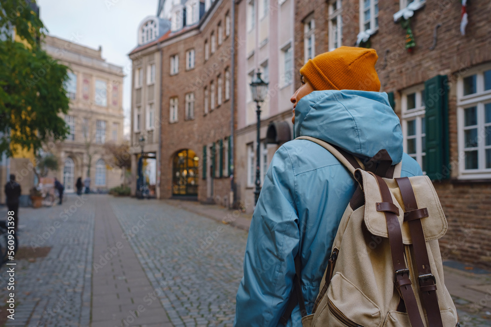 winter travel to Dusseldorf, Germany. young Asian tourist in blue jacket and yellow hat (symbol of Ukraine) walks through sights of old town or Altstadt. Popular center of Rheinland and Westphalia winter travel to Dusseldorf, Germany. young Asian tourist in blue jacket and yellow hat (symbol of Ukraine) walks through sights of old town or Altstadt. Popular center of Rheinland and Westphalia