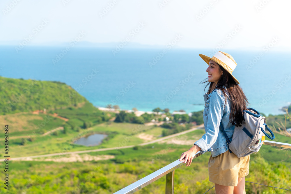 Asian woman with backpack solo travel on tropical island mountain peak in summer sunny day. Attractive girl enjoy and fun outdoor lifestyle looking beautiful nature of ocean on beach holiday vacation.