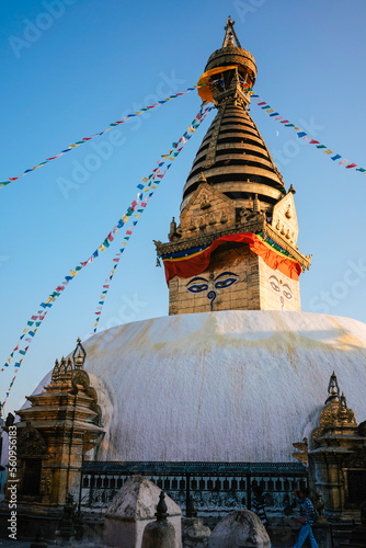 View of the Monkey Temple Stupa in Kathmandu Nepal against a blue sky in the warm evening light. The prayer flags are waving in the wind.