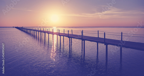 Wooden pier silhouette at sunrise, color toning applied.
