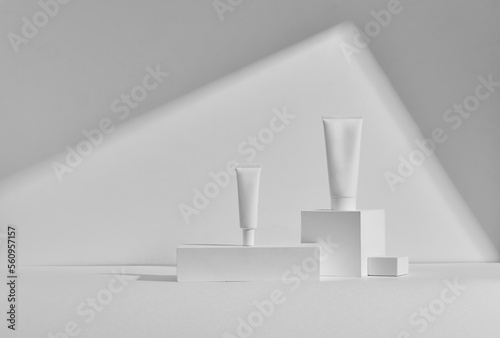 two white tubes of cosmetic cream on podiums and white background with shadow
