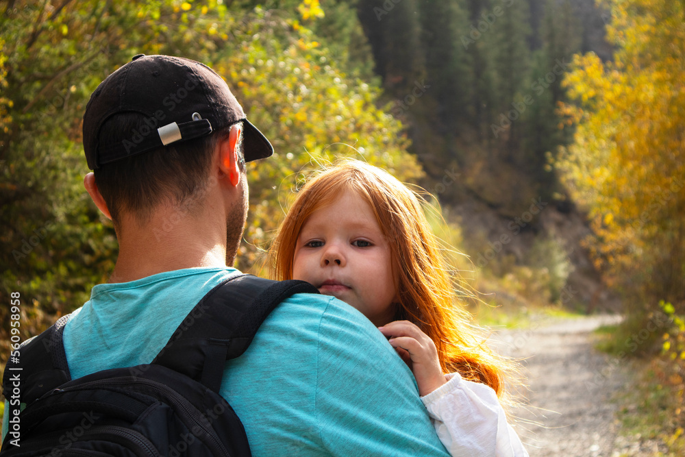 Fototapeta premium Dad carries his little daughter in his arms through the park