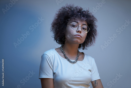 Close-up face portrait of cool kazakh model girl with curls and chain in neon light isolated on studio background