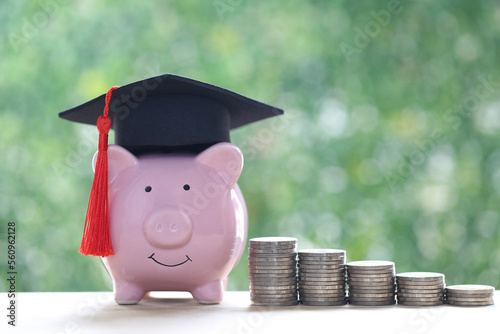 Graduation hat on piggy bank with stack of coins money on natural green background, Saving money for education concept